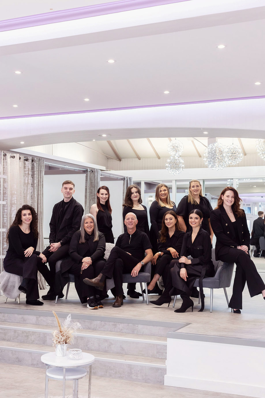 a group photo of eleven people, two men, nine women, all smiling and dressed in black, some sitting and some standing 