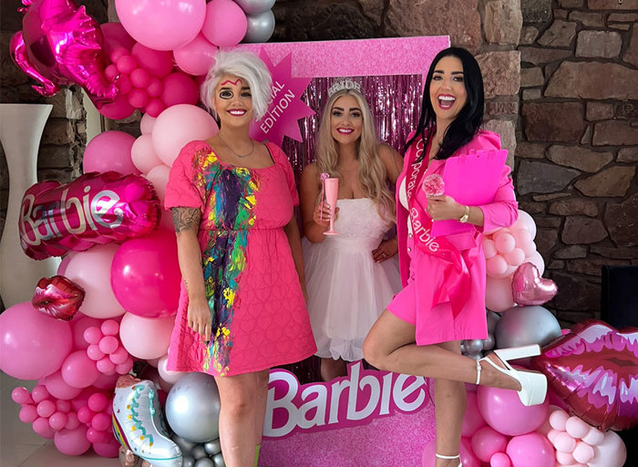 Three women dressed up as Barbie standing in front of pink balloon display