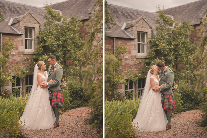 A bride in a white dress and a groom in a red tartan kilt and green jacket stand in front of a cottage 