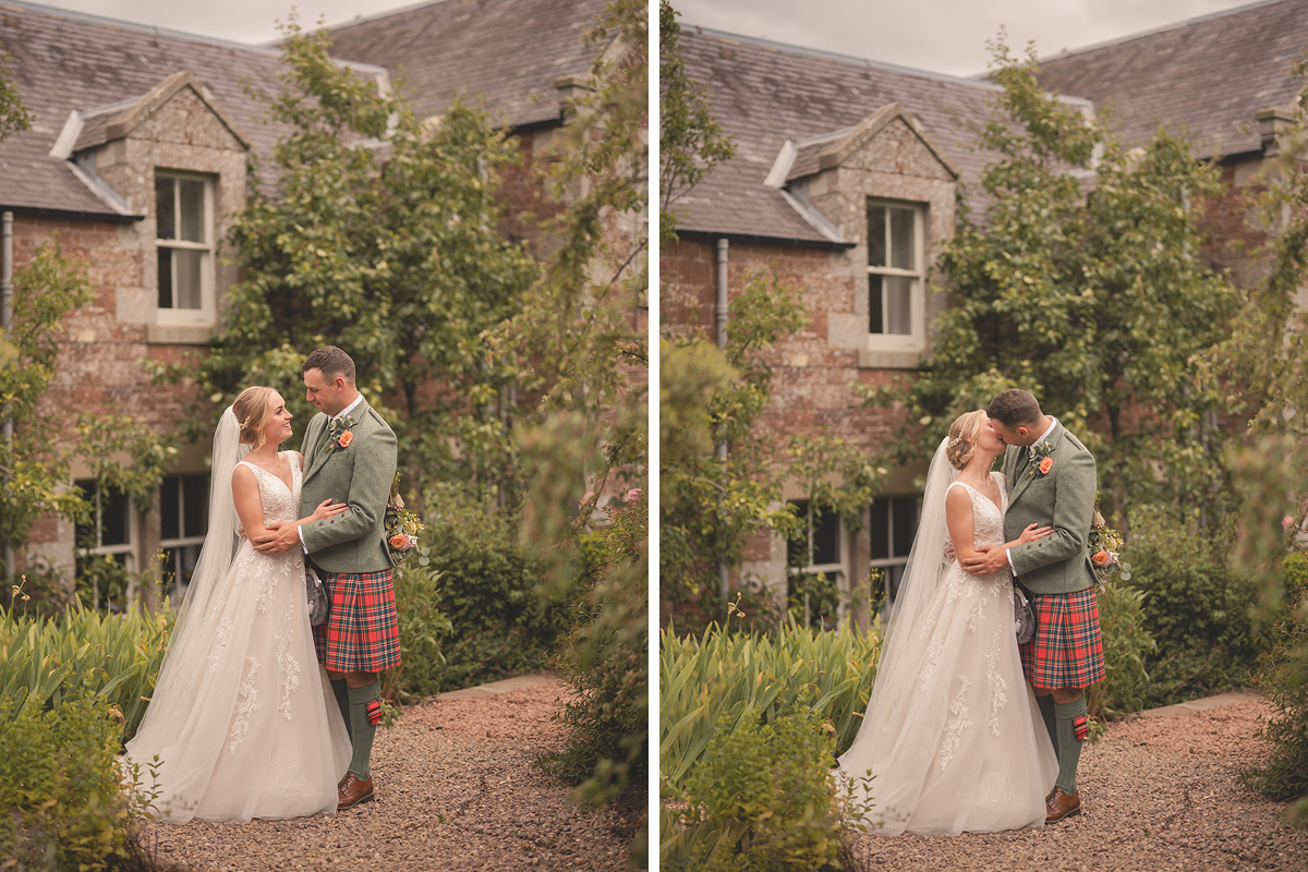 A bride in a white dress and a groom in a red tartan kilt and green jacket stand in front of a cottage