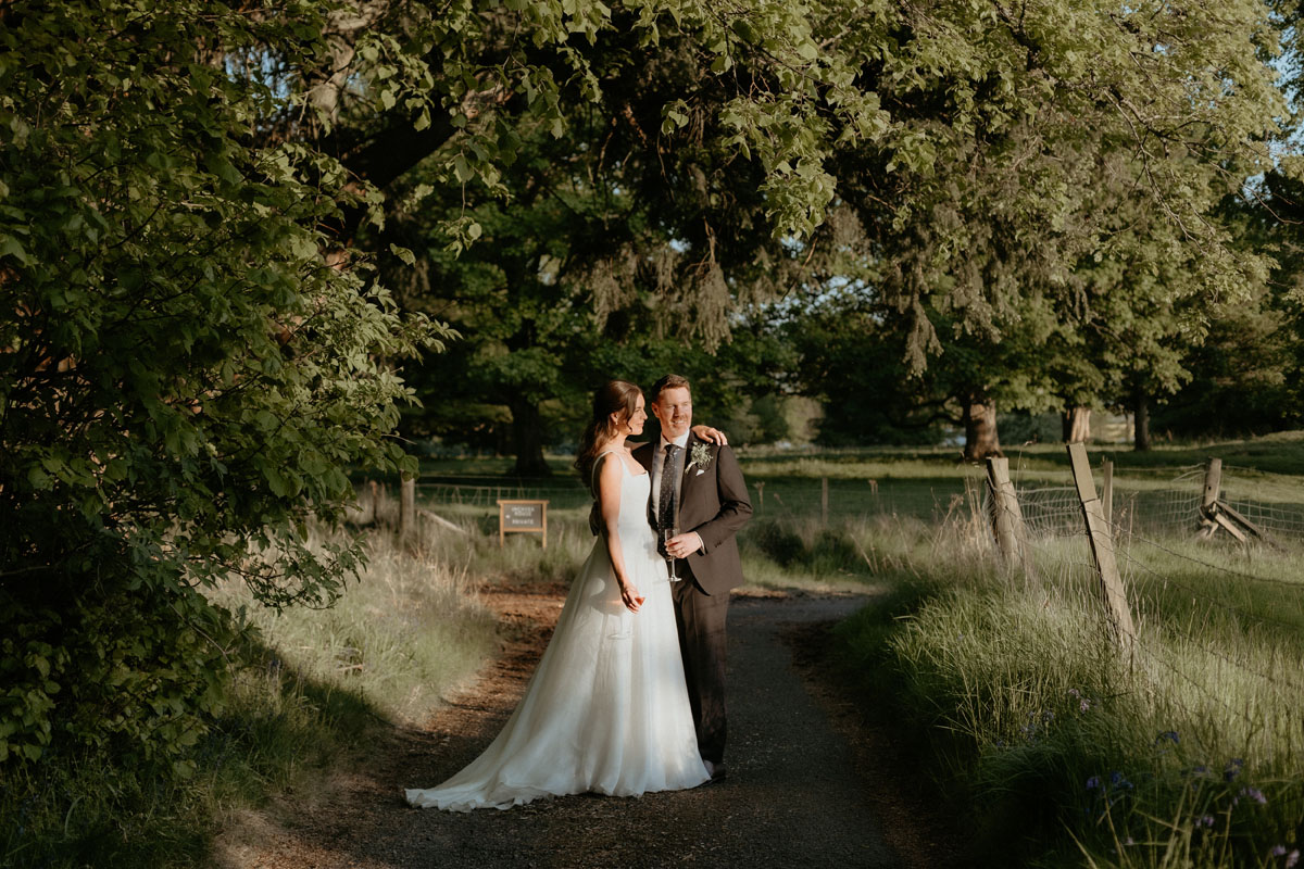 Newlyweds standing together on a tree-lined path at The Byre at Inchyra during their Perthshire wedding.