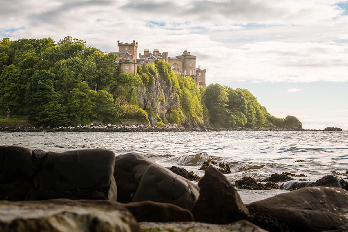 Culzean Castle perched on a clifftop overlooking the sea, surrounded by dense green woodland.