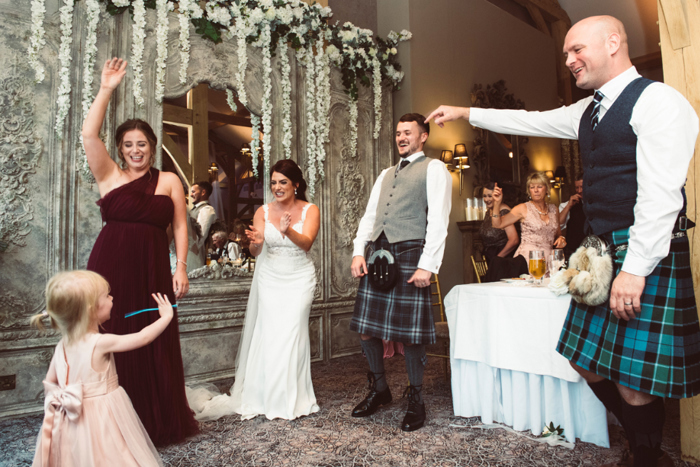 Bride, groom and guests dance with small girl in pink dress