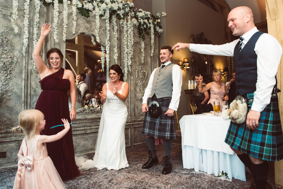Bride, groom and guests dance with small girl in pink dress