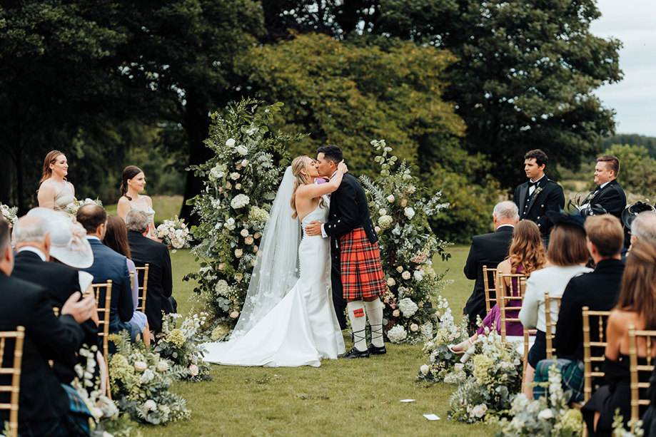 A bride and groom kissing in during a wedding ceremony in a garden.