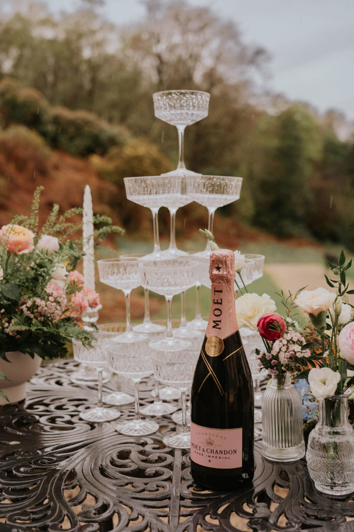 A metal black table with a champagne tower on it and a bottle of Moet Rose Imperial sitting in front of the tower