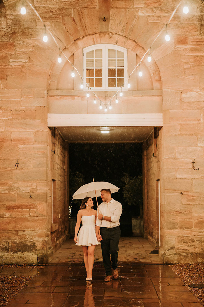 a bride and groom under an ivory umbrella and festoon lighting at night at Dunglass Estate