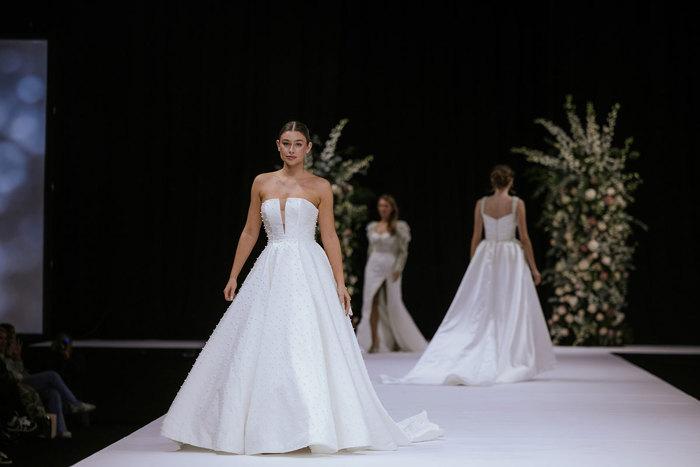 A person in a white dress walking on a white catwalk.