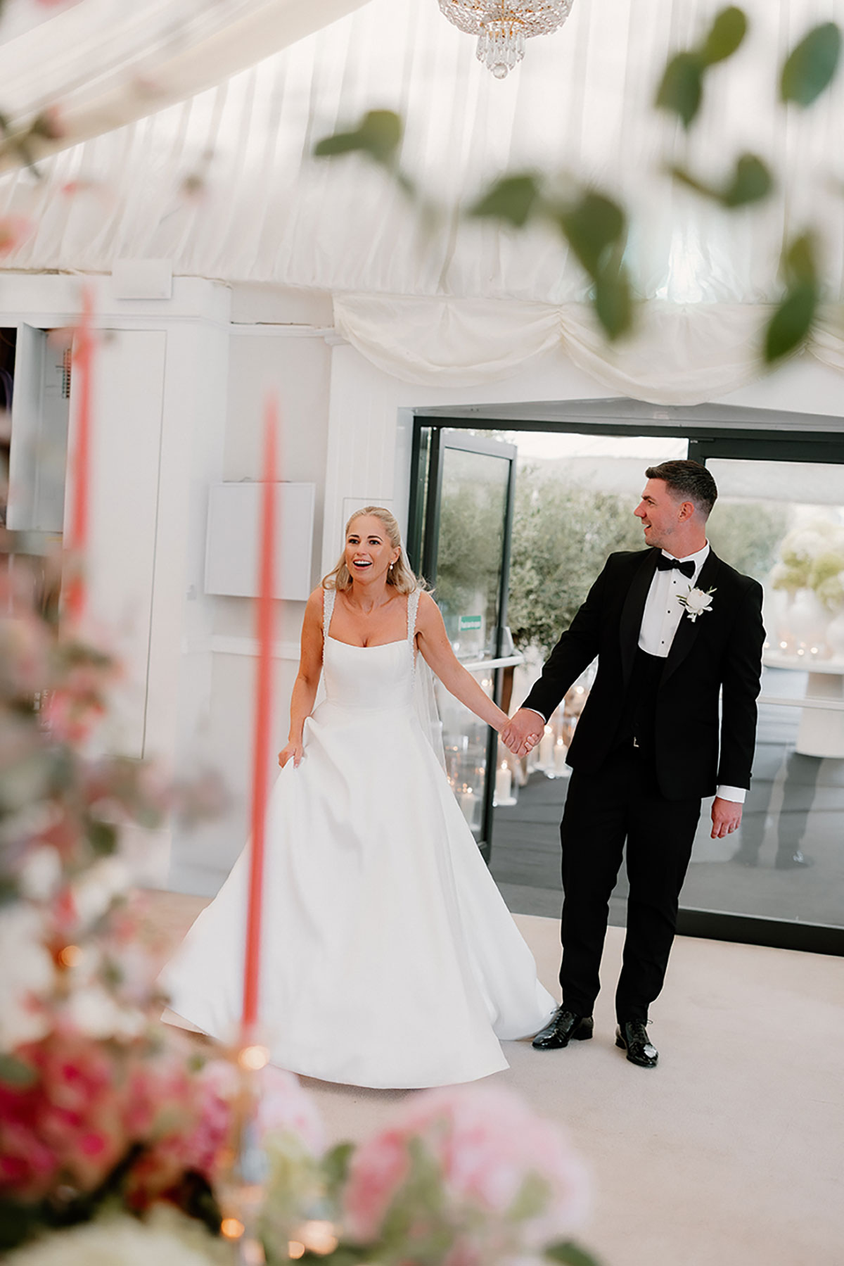 Bride and groom entering the wedding reception marquee hand in hand, smiling as they see the decor.