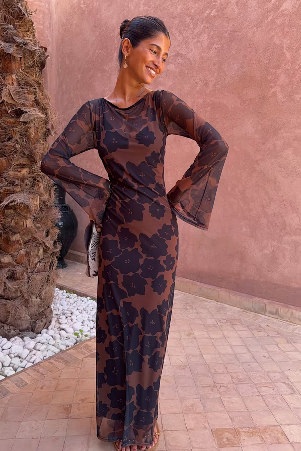 Woman wearing a brown floral maxi dress with sheer flared sleeves and a fitted silhouette.