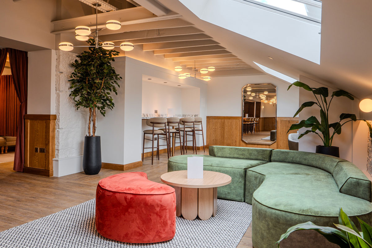 A contemporary lounge with curved green seating, a red accent stool and a small bar area.