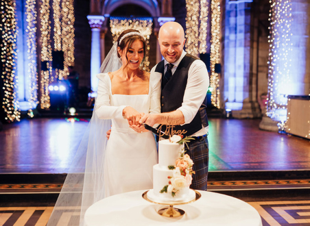 couple cutting wedding cake smiling on dancefloor in front of twinkling fairy lights