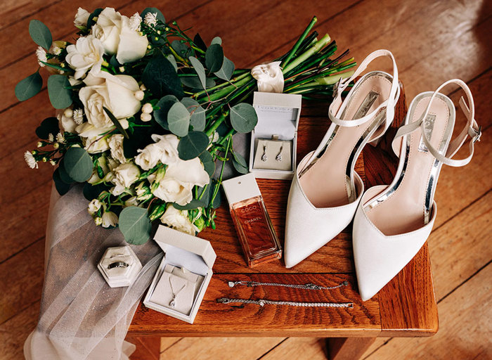 shoes, perfume, jewellery and a bridal bouquet on a wooden table