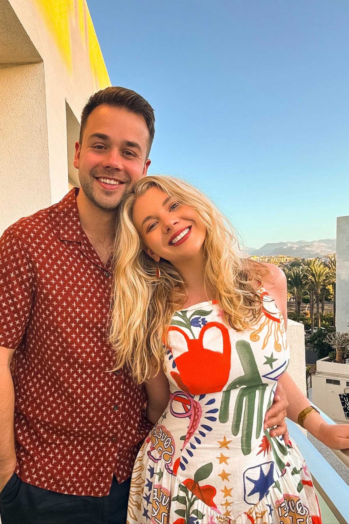 Smiling couple posing together on a sunny balcony with mountain views in the background
