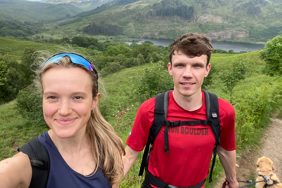 Couple hiking in the Scottish Highlands with a dog on a scenic hillside trail overlooking a loch and green valley