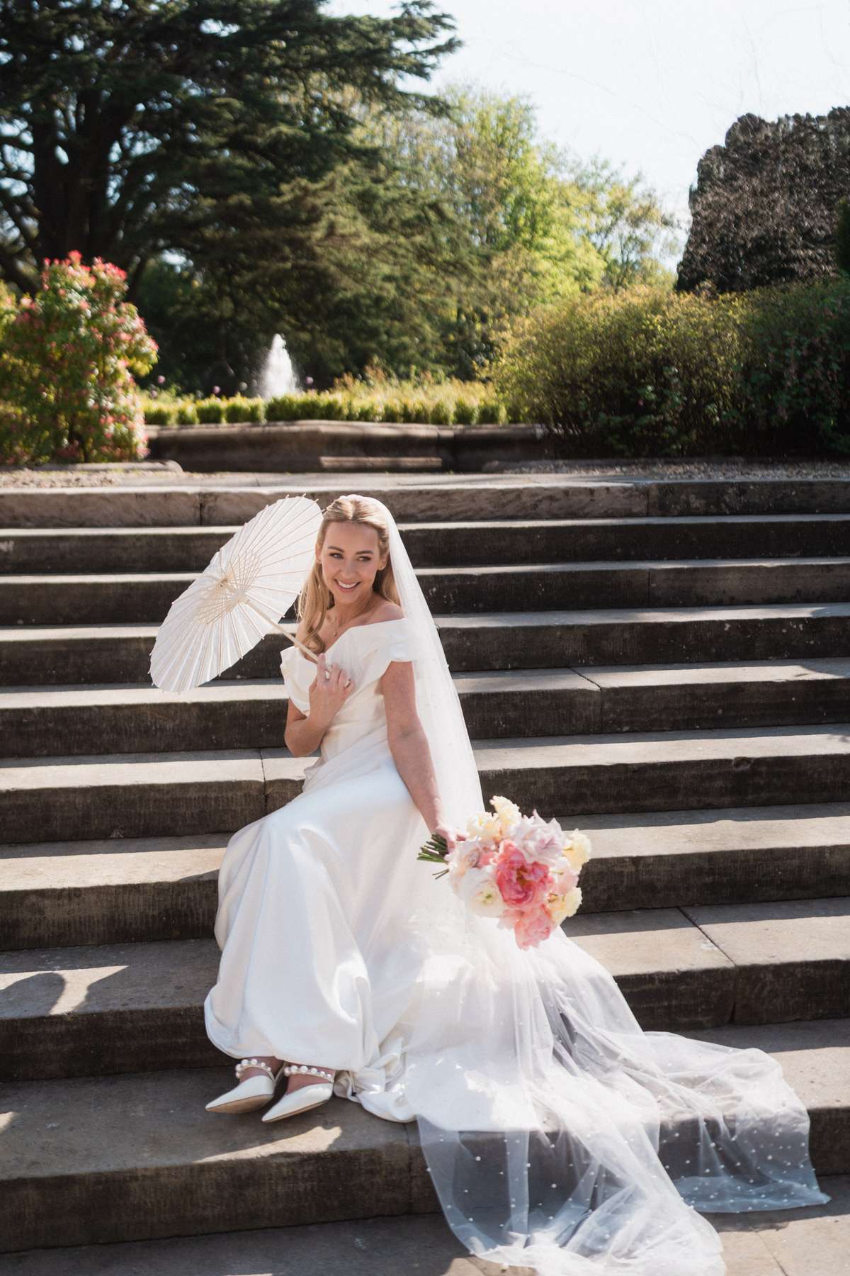 Bride Siân poses with a white parasol and pastel pink bouquet on the garden steps at Mar Hall in Renfrewshire.