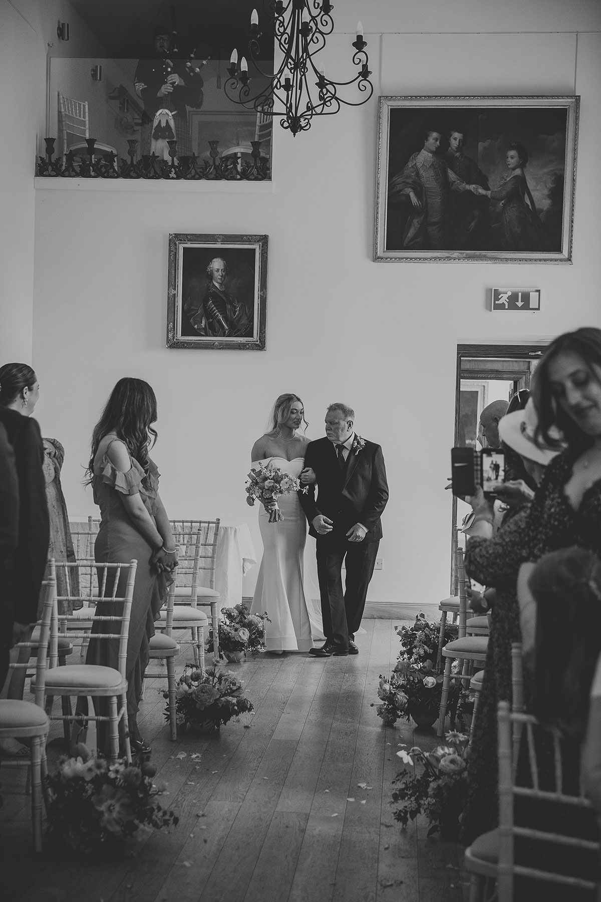 Bride walking down aisle with father during indoor wedding ceremony with floral aisle decor