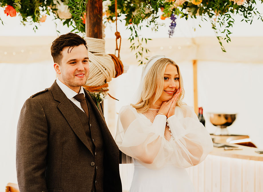 a bride and groom look emotional in a marquee with flower decoration hanging above them