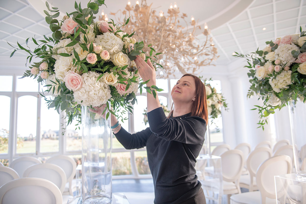 Wedding florist arranging pastel pink and white flowers for a luxury ceremony setup