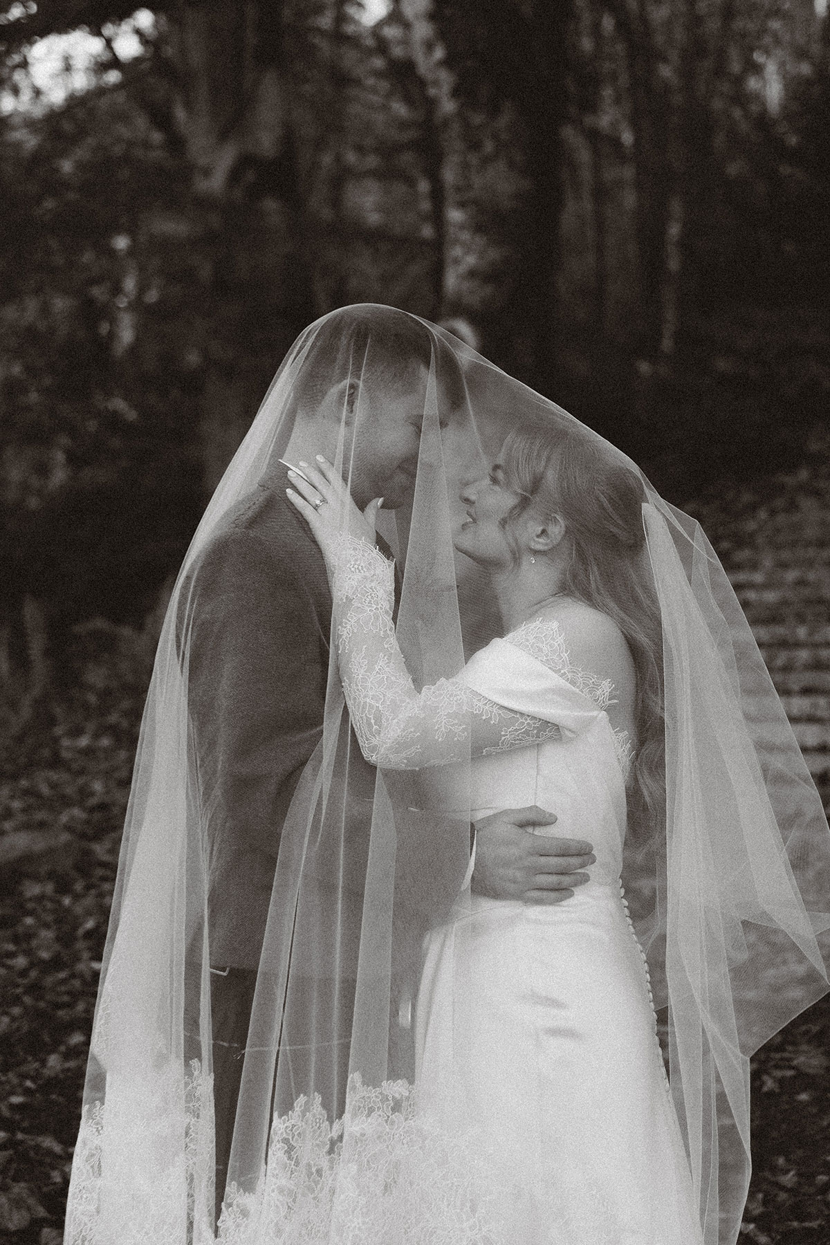 Black and white portrait of bride and groom kissing under veil in romantic woodland Scottish wedding setting