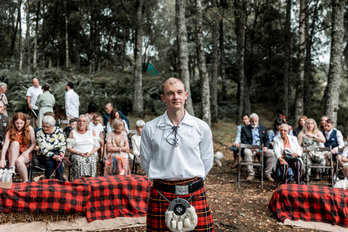 Groom wearing kilt waits at the top of the aisle