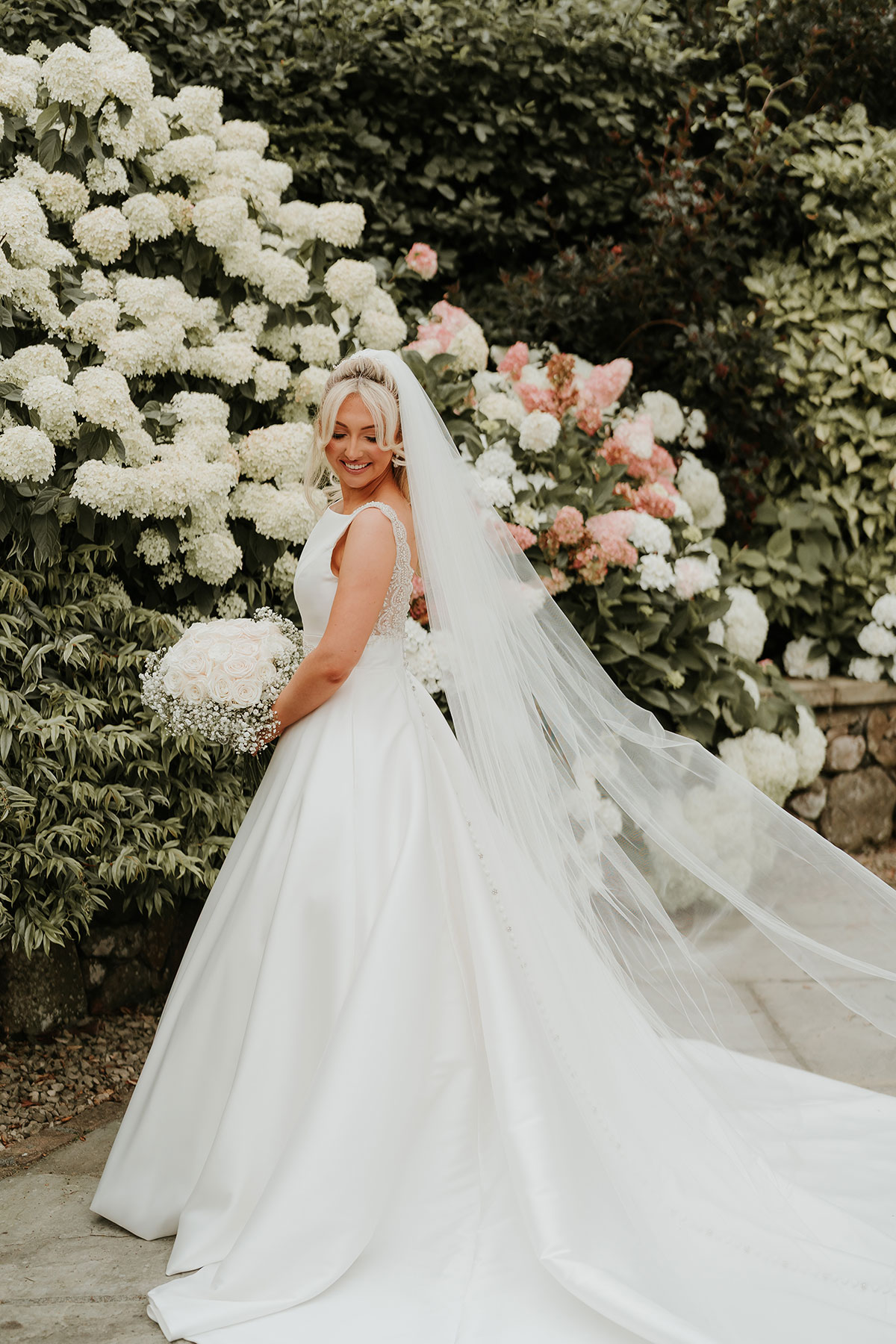 Bride holding bouquet beside white and blush hydrangeas at Ingliston Country Club wedding gardens