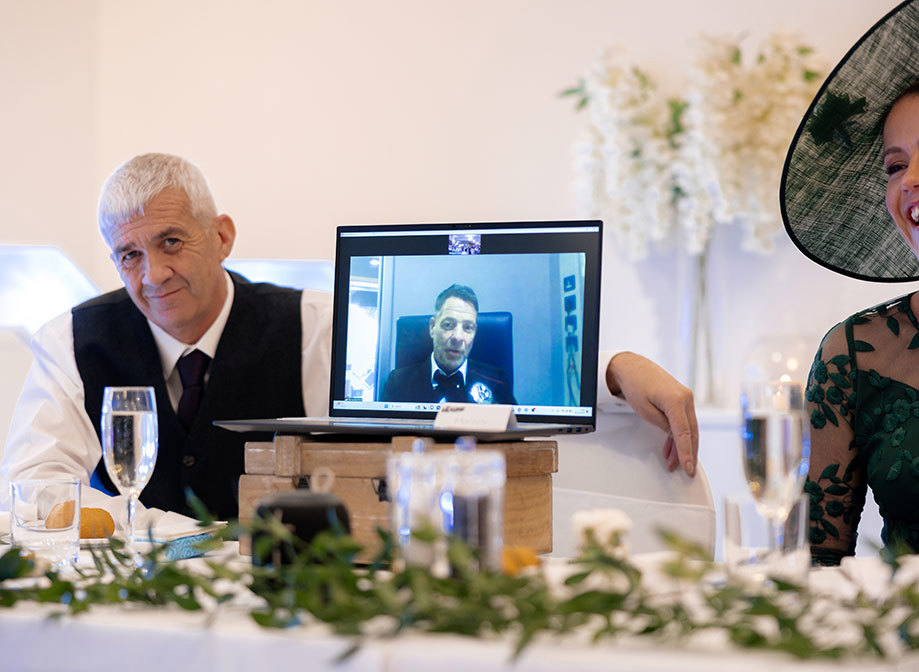 a laptop with a person on video call sitting on a top table at a wedding