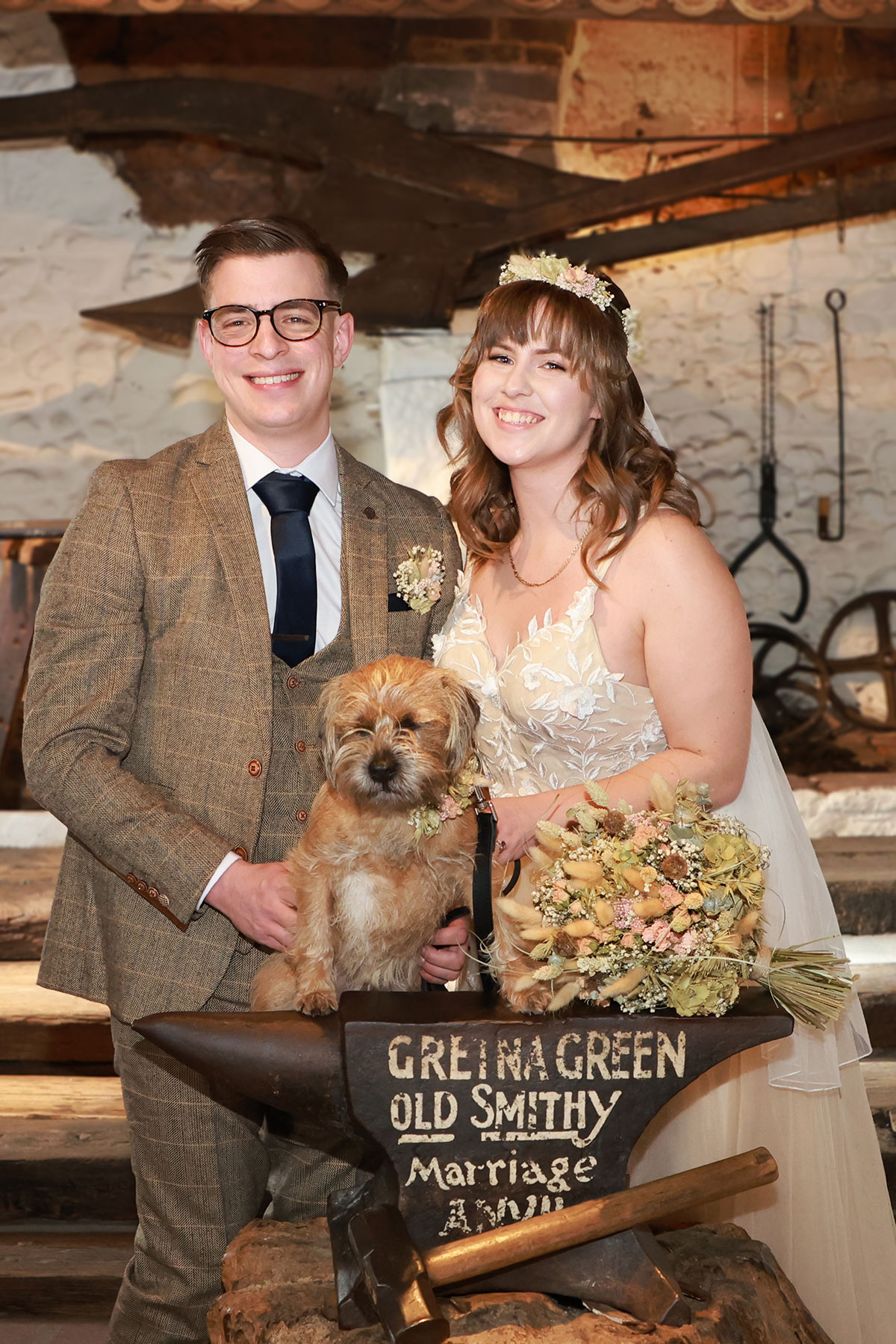 couple smile with dog next to gretna green sign on wedding day