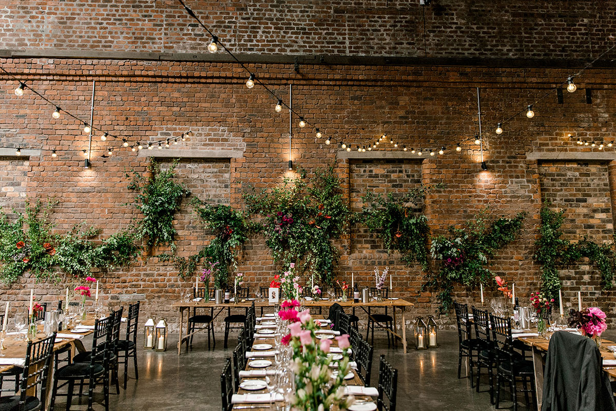 Industrial wedding reception space with exposed brick walls, long tables and hanging festoon lights