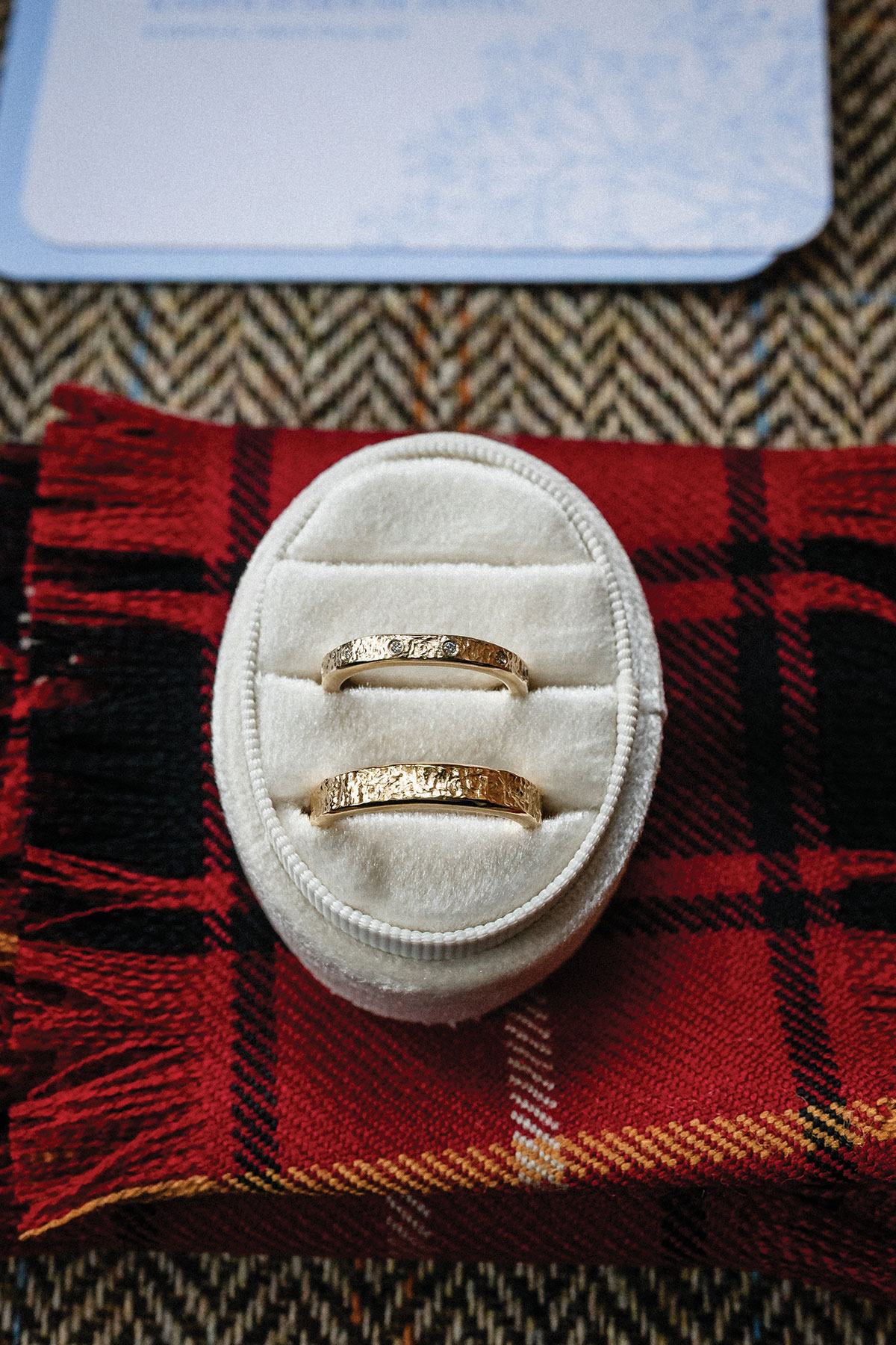 Textured gold wedding rings by Sheila Fleet displayed in a white velvet ring box on red tartan fabric.