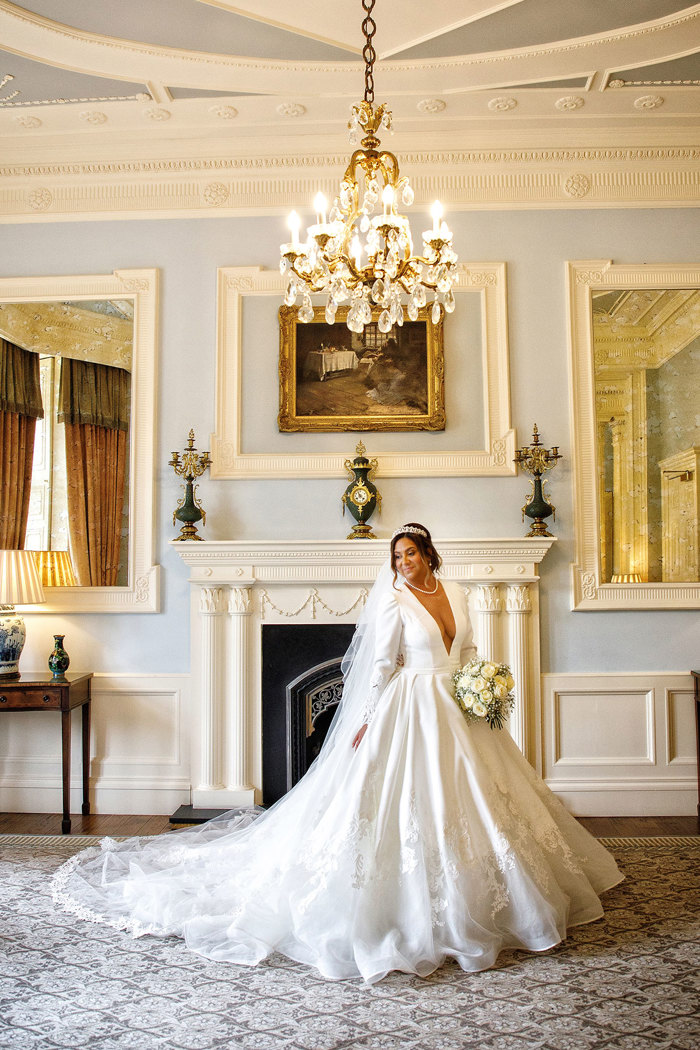 a bride posing by a grand fireplace in an elegant room.