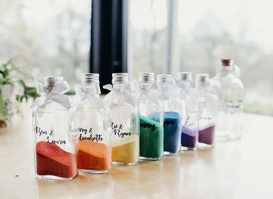 a line up of glass bottles personalised with people's names containing different colours of sand