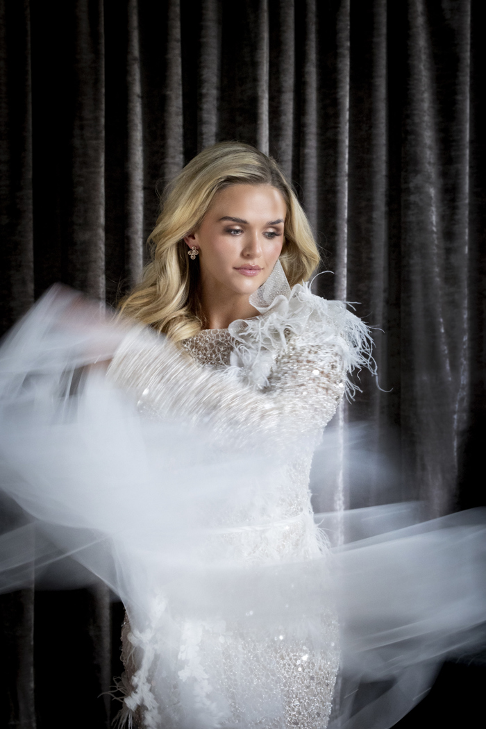 A blonde woman wearing a sparkly white dress swooshing the fabric across the camera with her left arm