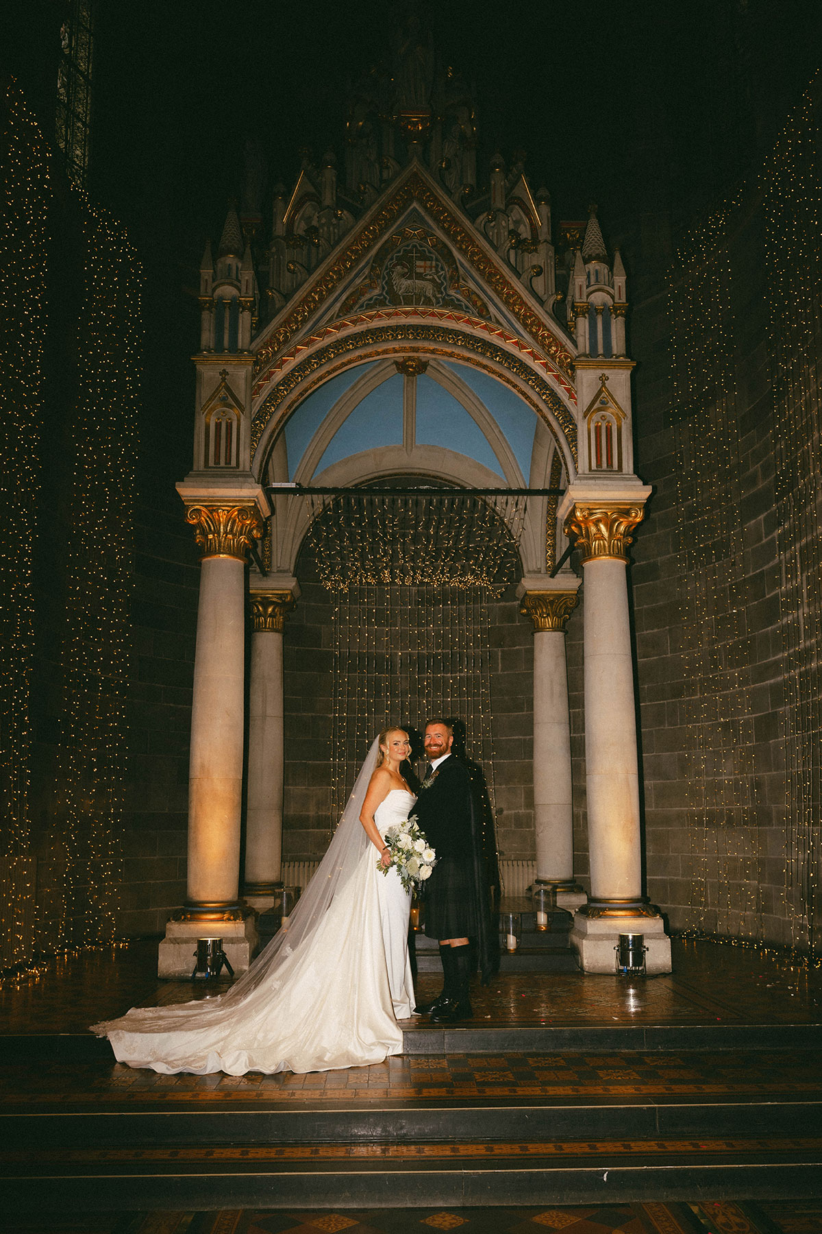 bride and groom standing together under decorative arch with fairy lights backdrop