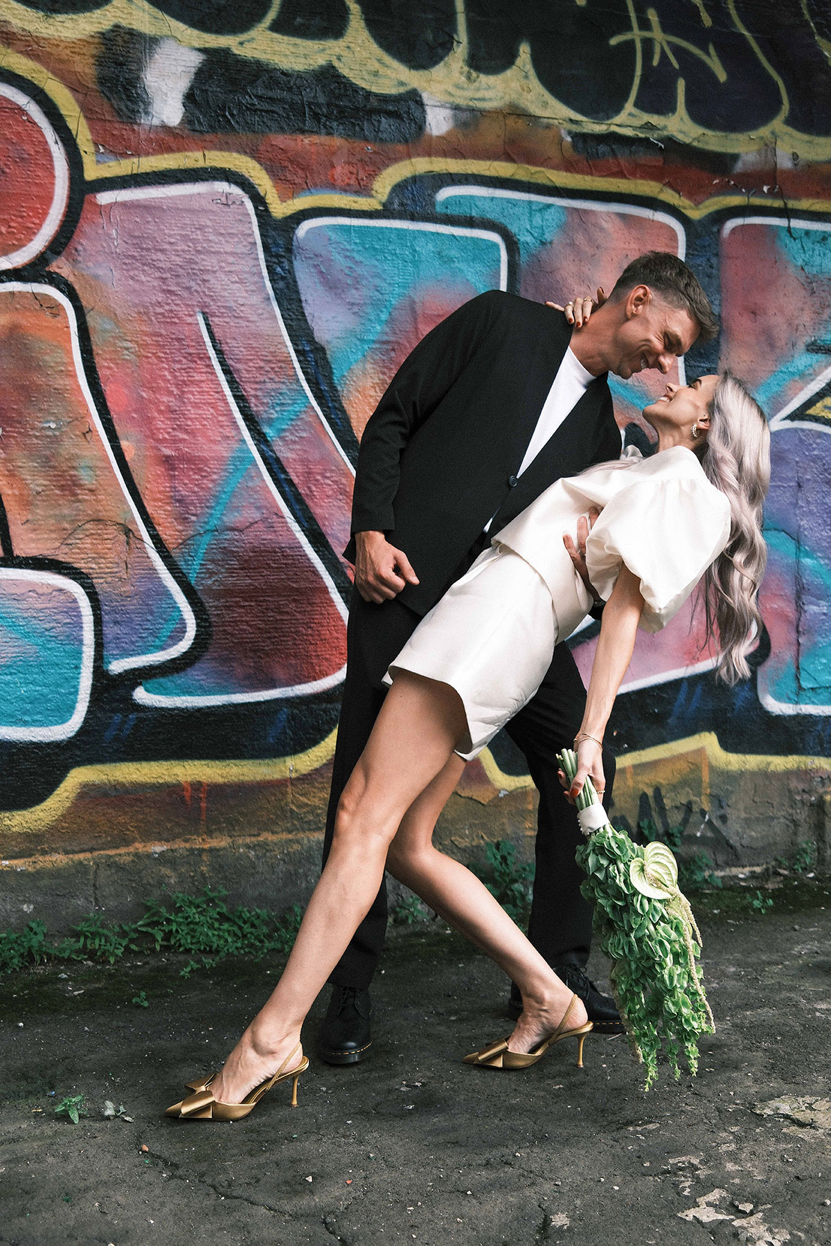 Bride and groom posing beside colourful Glasgow street art after relaxed city wedding ceremony
