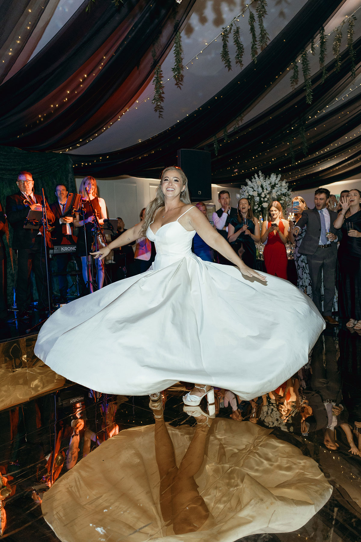 Bride twirls on gold mirrored dancefloor under chandeliers during Dundas Castle wedding reception.