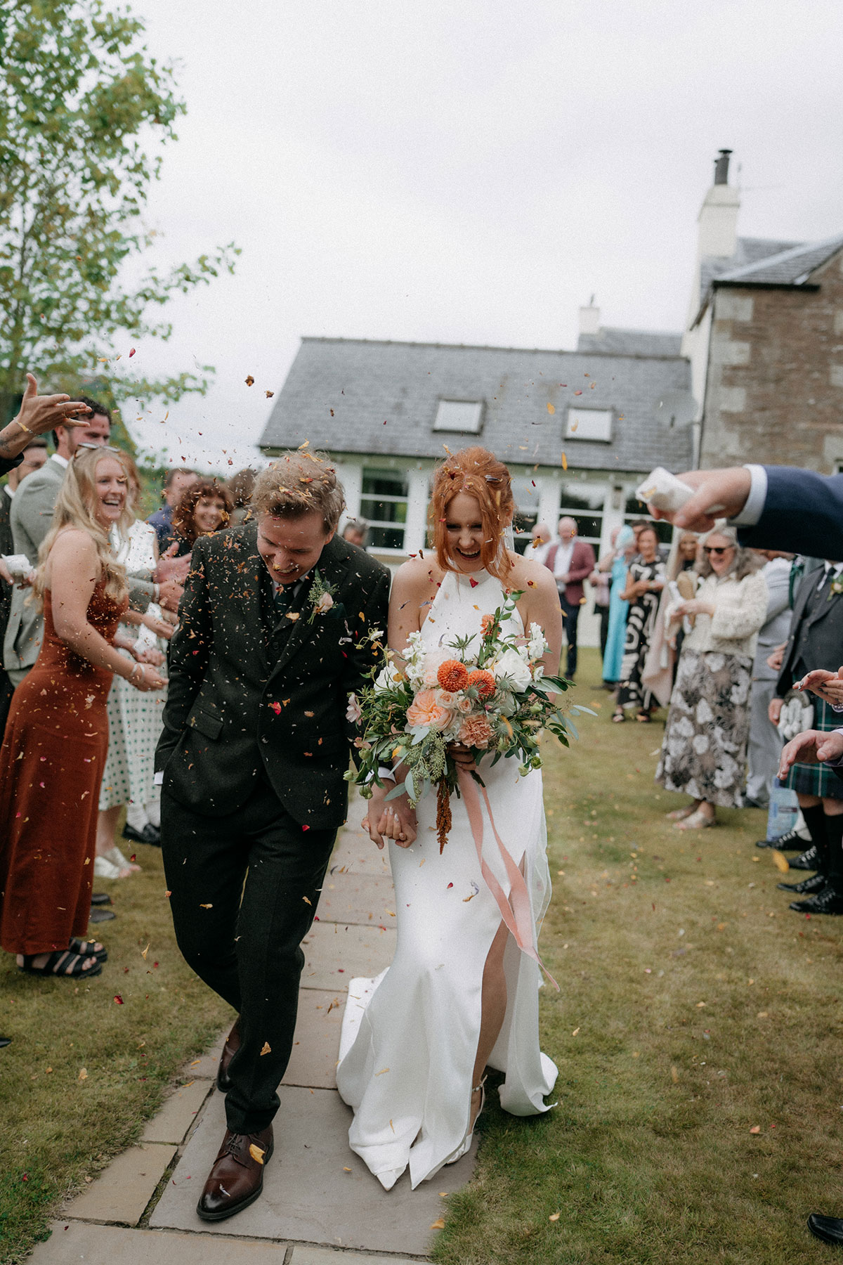 Bride and groom walking through confetti after outdoor wedding ceremony holding bouquet