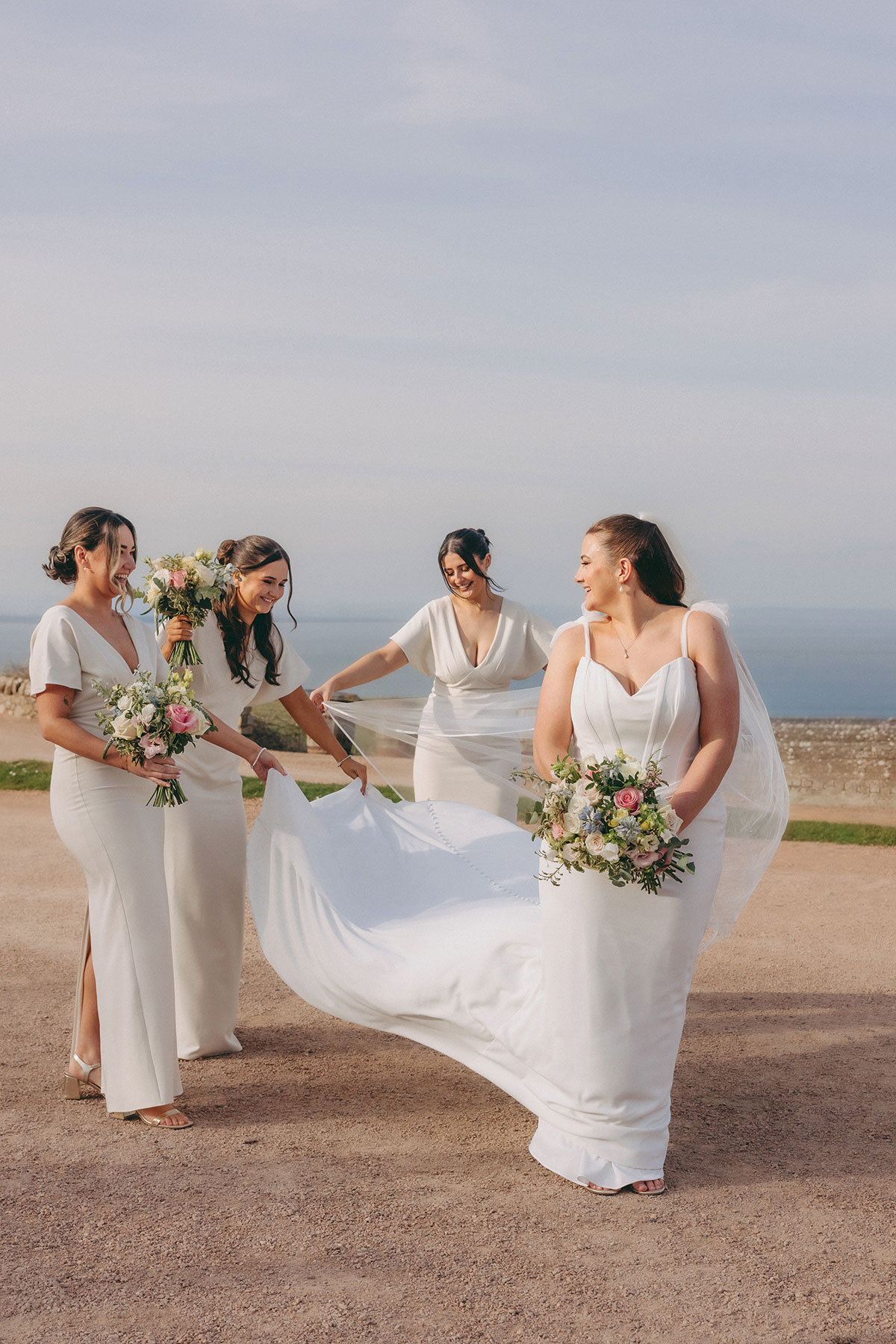 Bride with three bridesmaids dressed in white and champagne tones during an outdoor Scottish wedding portrait.