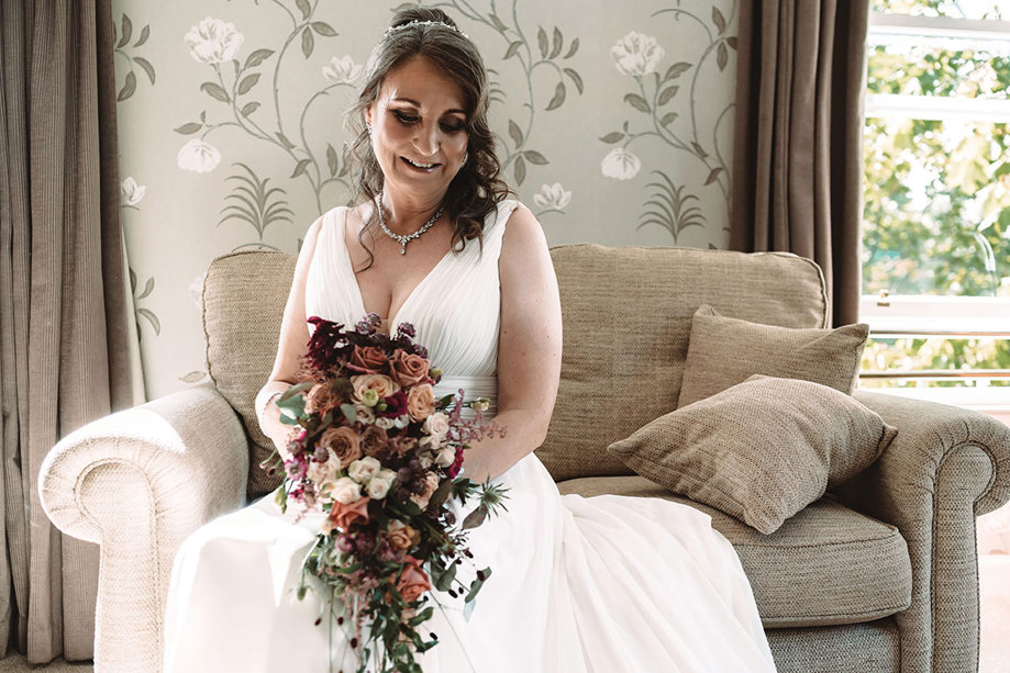 bride sits on sofa holding a cascading bouquet