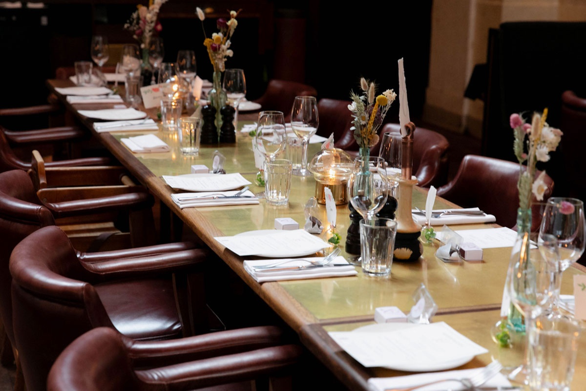 Long wedding dining table at Hawksmoor Edinburgh with candles, flowers, menus and leather chairs.