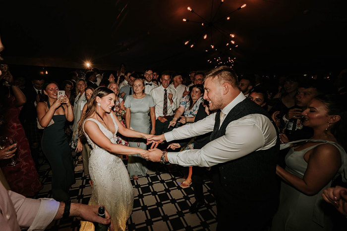 a bride and groom holding hands dancing surrounded by guests during a wedding reception at Dunglass Estate