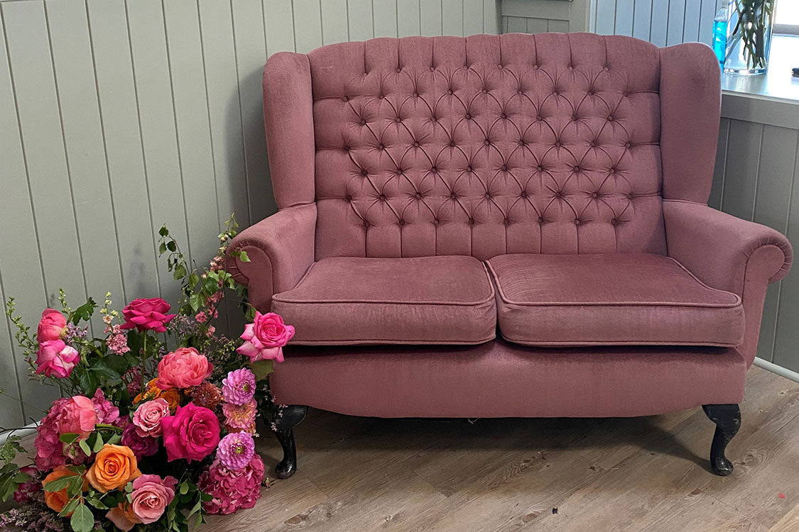pink loveseat sofa with a bouquet of pink and orange flowers on the floor next to it