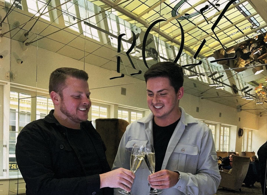 two men clinking champagne flutes in front of a mirror at ROX in Glasgow