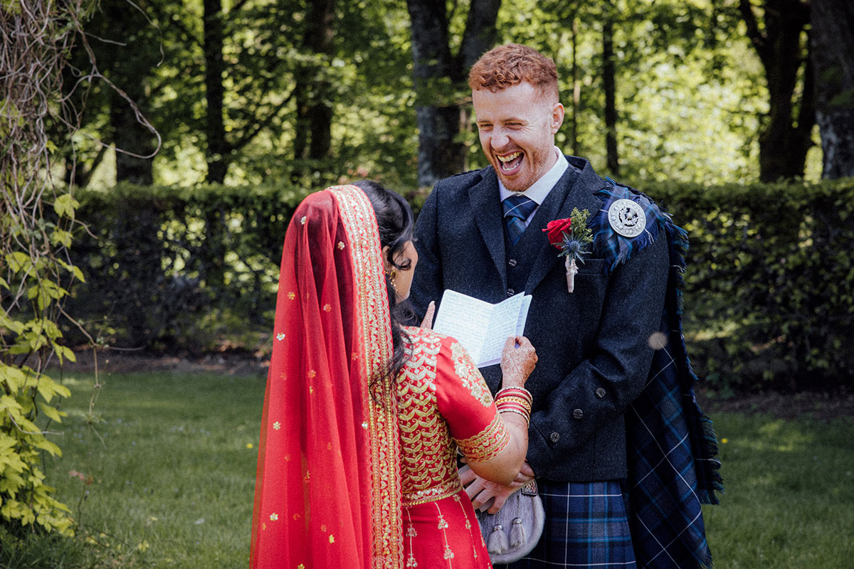 Bride reading her vows as the groom laughs during an outdoor wedding ceremony at Atholl Palace Hotel in Perthshire