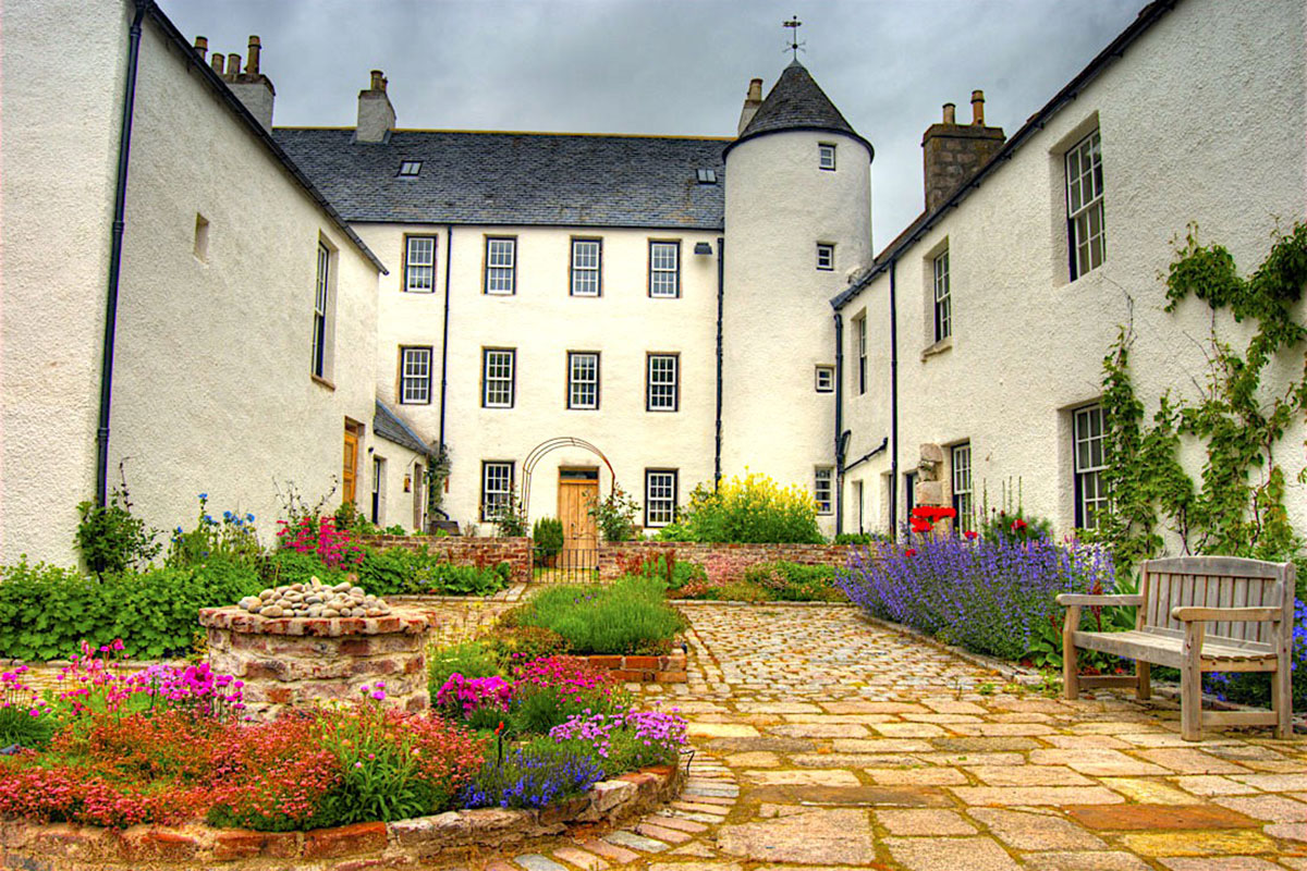 A courtyard garden with colourful planting, cobbled paths and the whitewashed exterior of Logie Country House.