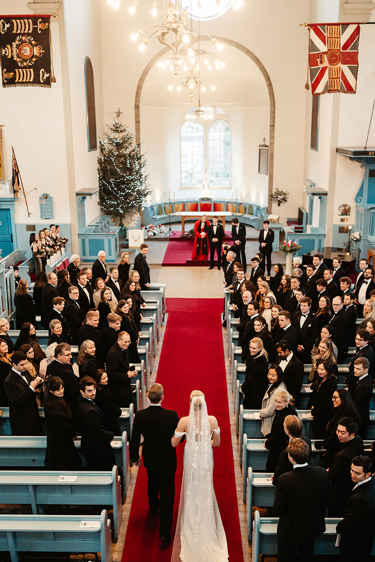 Bride walking up the red-carpeted aisle with her father in Canongate Kirk, guests turning to watch.