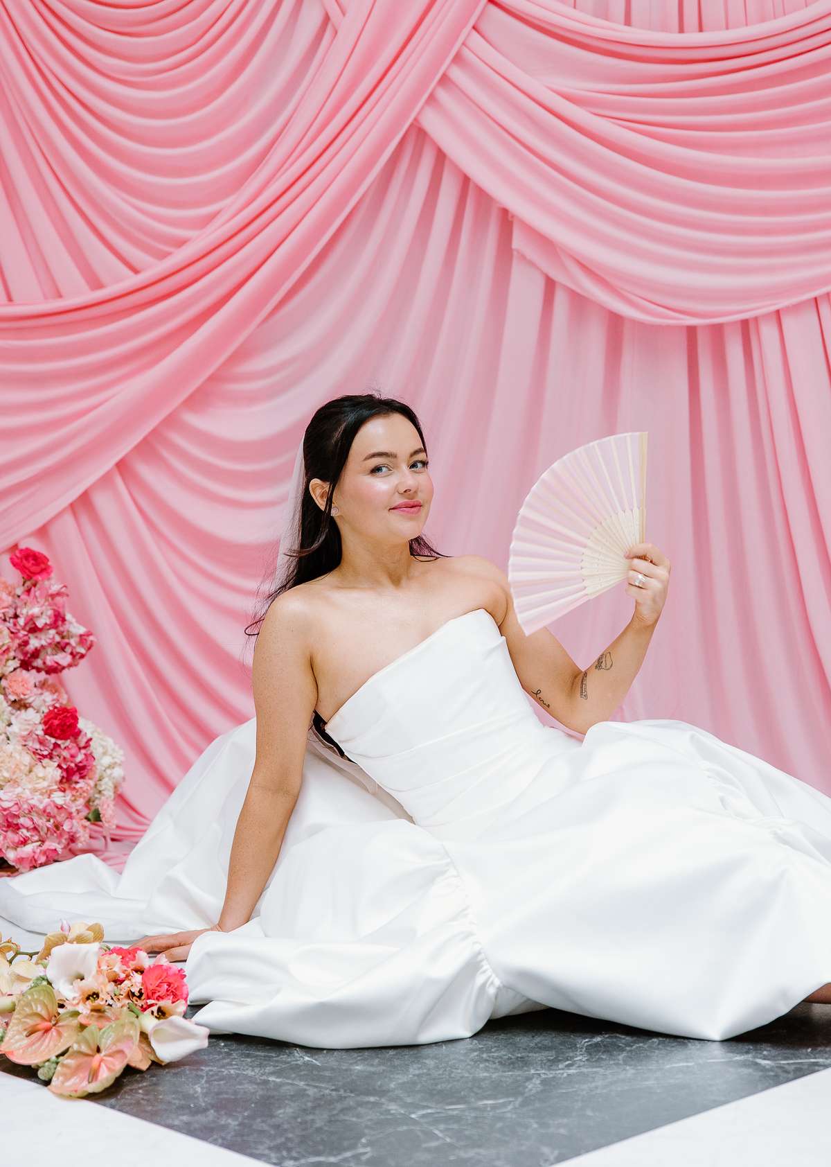 Bride poses with a fan in her strapless wedding dress against a statement pink draped backdrop at The Collector’s Hall Glasgow.