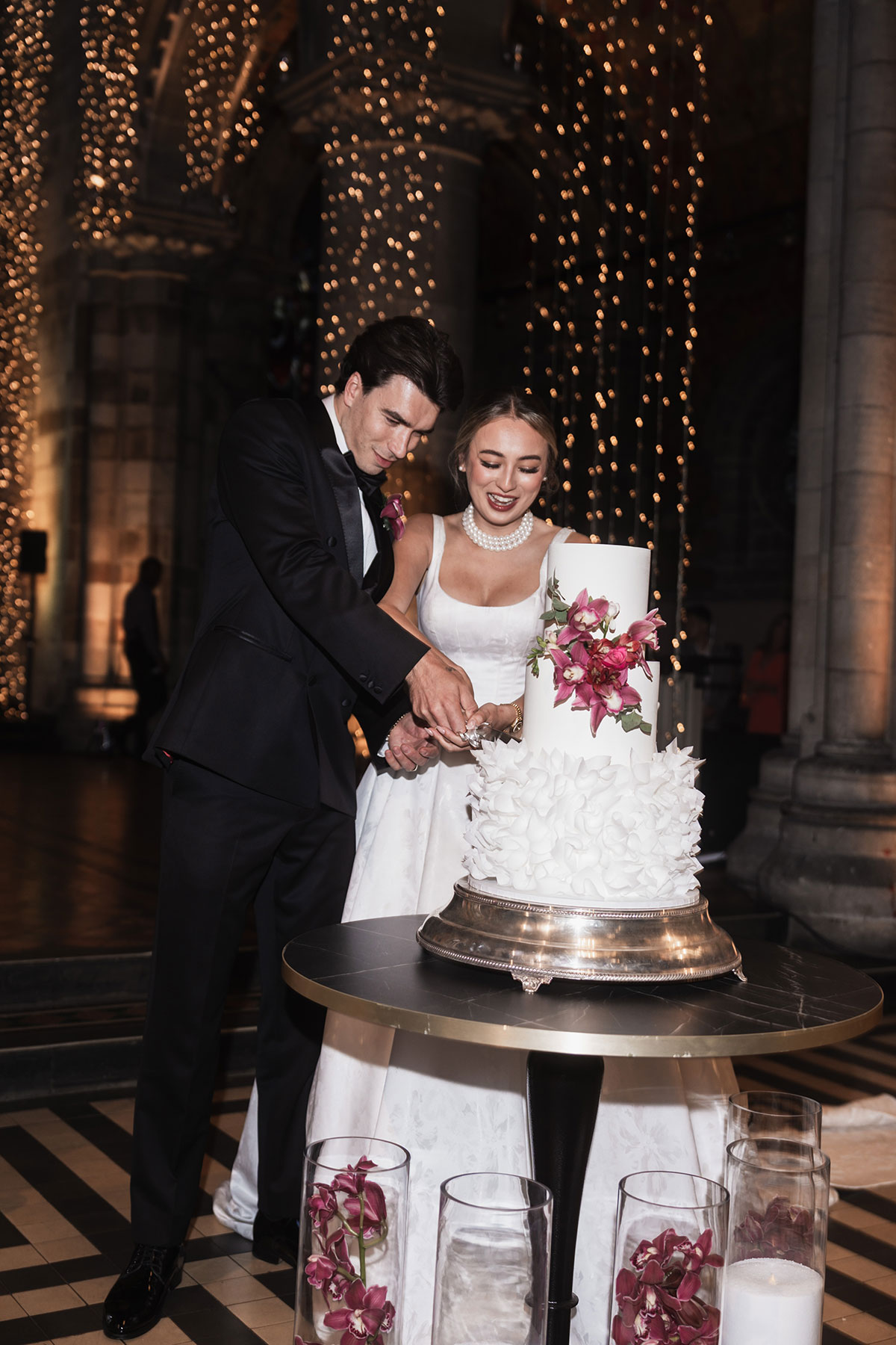 Bride and groom cutting a tiered white wedding cake with pink orchid flowers at Mansfield Traquair