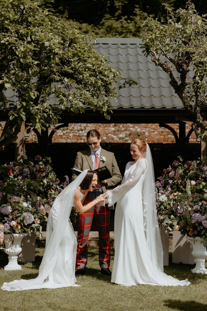 two brides holding hands in front of a celebrant during an outdoor wedding ceremony in the walled garden at two brides walking through a confetti shower during outdoor wedding at the Byre at Inchyra