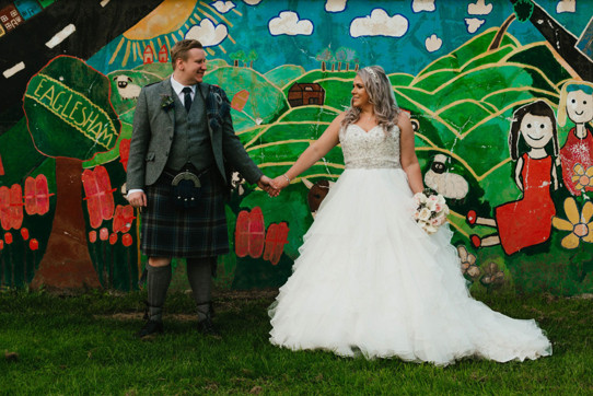 A Bride And Groom Standing In Front Of A Colourful Painted Mural Outdoors